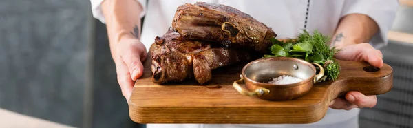 Cropped view of chef holding delicious meat on cutting board, banner — Stock Photo