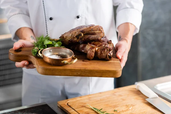 Ausgeschnittene Ansicht des Chefs, der in der Küche gebratenes Fleisch auf Schneidebrett hält — Stockfoto