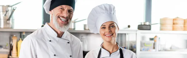 Chefs positivos sonriendo a la cámara en la cocina del restaurante, pancarta - foto de stock