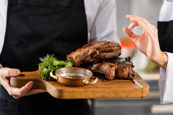 Ausgeschnittene Ansicht von Koch zeigt okay Geste nahe Kollege mit gebratenem Fleisch auf Schneidebrett — Stockfoto
