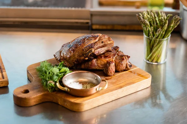 Delicious meat on cutting board near asparagus on table — Stock Photo