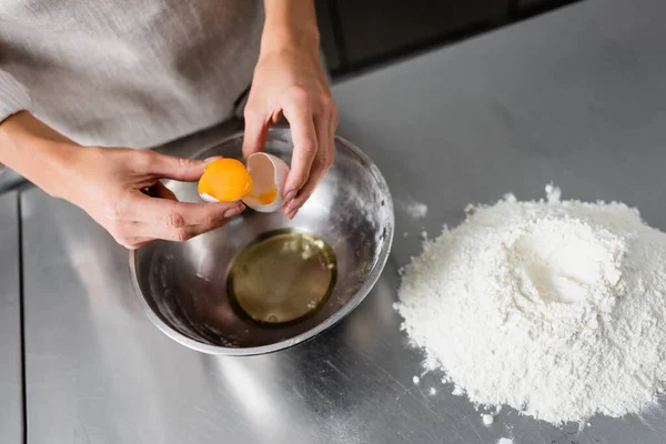 Zugeschnittene Ansicht des Chefs mit Ei und Eierschale in der Nähe von Schüssel und Mehl auf dem Tisch — Stockfoto