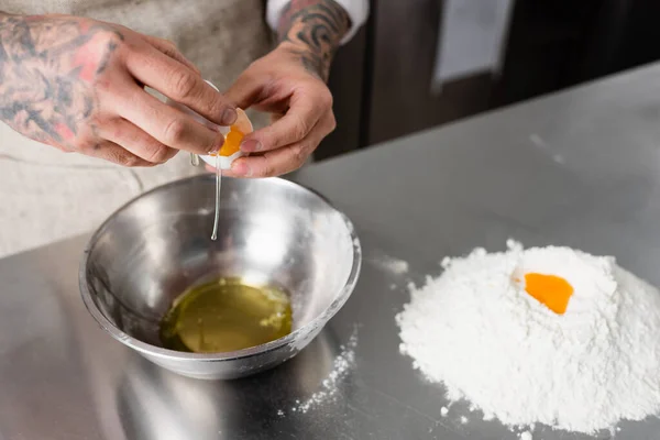 Ausgeschnittene Ansicht des Chefs, der Ei in der Nähe von Schüssel und Mehl auf dem Küchentisch hält — Stockfoto