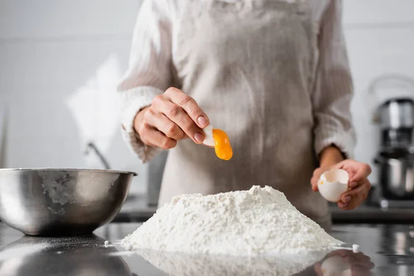 Vue recadrée du chef versant du jaune d'oeuf sur la farine sur la table de cuisine — Photo de stock