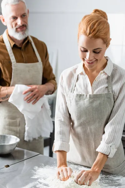 Smiling chef making dough near blurred colleague with towel in kitchen — Stock Photo