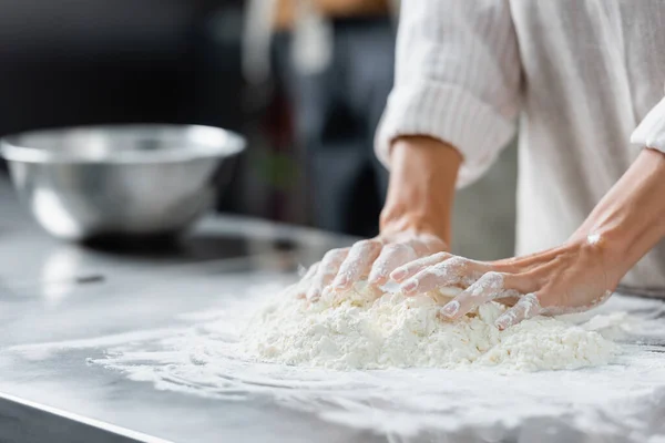 Cropped view of chef making dough near blurred bowl on kitchen table — Stock Photo