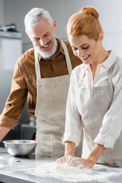 Chef alegre en delantal haciendo masa cerca de colega borrosa en la cocina - foto de stock