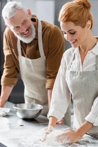 Chef haciendo masa cerca borrosa sonriente colega en la cocina - foto de stock