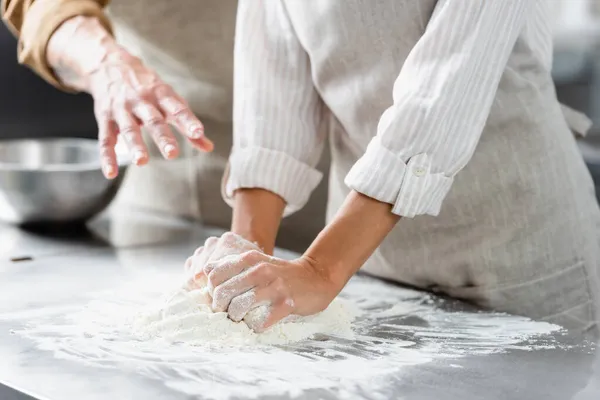 Vue recadrée du chef faisant la pâte près de son collègue pointant la main dans la cuisine — Photo de stock