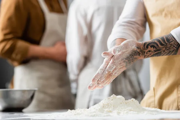 Обрізаний вид татуйованого шеф-кухаря, що стоїть біля борошна на столі на кухні — стокове фото