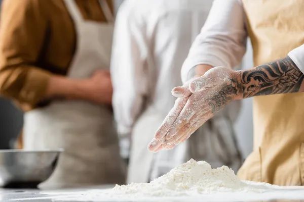 Ausgeschnittene Ansicht tätowierter Koch, der in der Nähe von Mehl auf dem Tisch in der Küche steht — Stockfoto