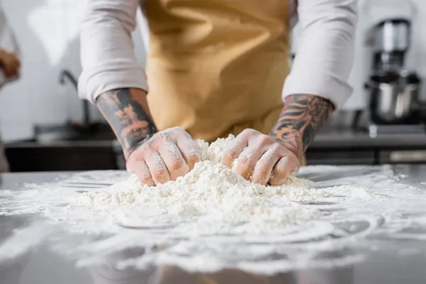 Vista cortada de chef tatuado fazendo massa perto de farinha desfocada na cozinha — Fotografia de Stock