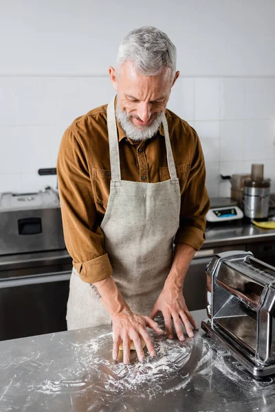 Зрелый шеф-повар делает тесто возле машины для приготовления макарон на кухне — стоковое фото
