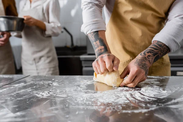 Vista ritagliata dello chef tatuato che fa pasta vicino a colleghi sfocati in cucina — Foto stock