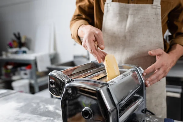 Vista cortada do chef em avental colocando massa na máquina de fazer macarrão na cozinha — Fotografia de Stock