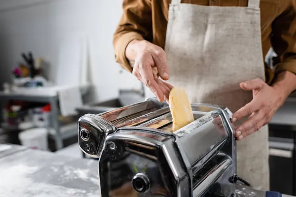 Ausgeschnittene Ansicht des Chefs in der Schürze, die Teig in Nudelmaschine in der Küche setzt — Stockfoto