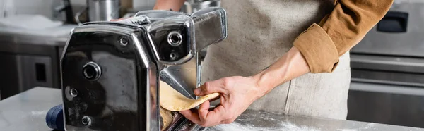 Обрезанный вид шеф-повара в фартуке держа тесто возле машины производителя макарон на кухне, баннер — стоковое фото