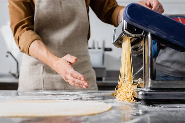 Vista recortada del chef en delantal haciendo espaguetis en la máquina de hacer pasta - foto de stock