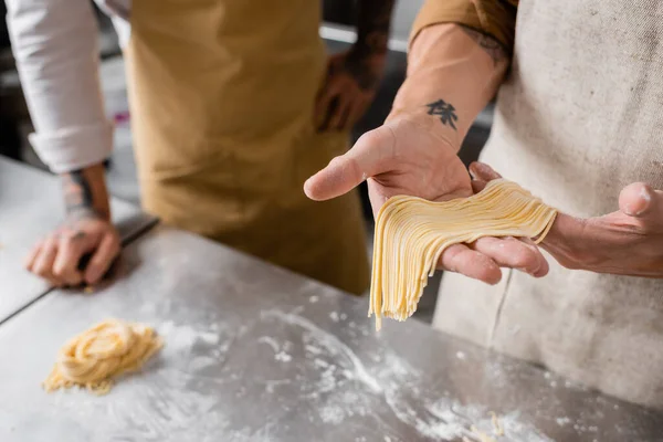 Cropped view of chef holding raw spaghetti near colleague in kitchen — Stock Photo