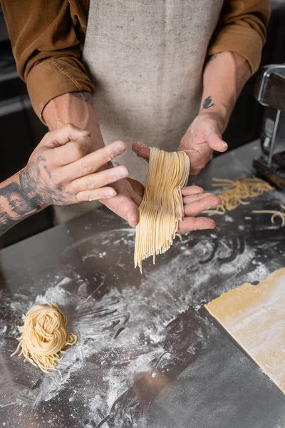 Vista recortada de chef tatuado mostrando gesto ok cerca de colega con espaguetis crudos en la cocina - foto de stock