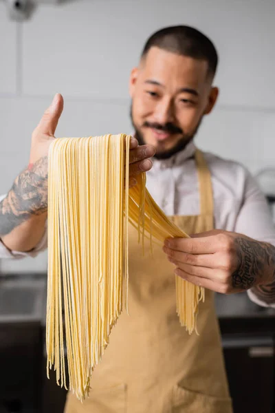 Chef asiático em avental segurando espaguete cru na cozinha — Fotografia de Stock