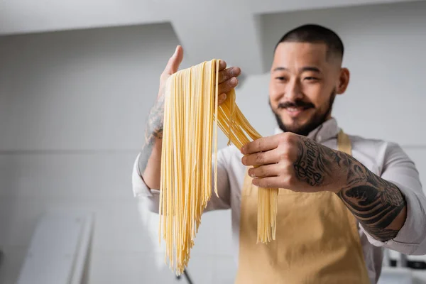 Los espaguetis crudos en las manos del chef alegre asiático en la cocina - foto de stock