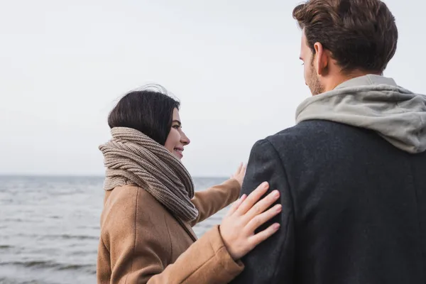 Vista trasera del hombre cerca de la mujer señalando con la mano en el mar durante el paseo de otoño - foto de stock