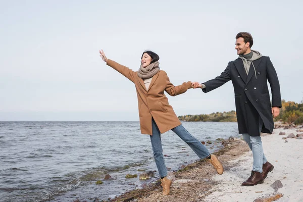 Femme joyeuse agitant la main tout en marchant et en s'amusant avec petit ami près de la mer — Photo de stock