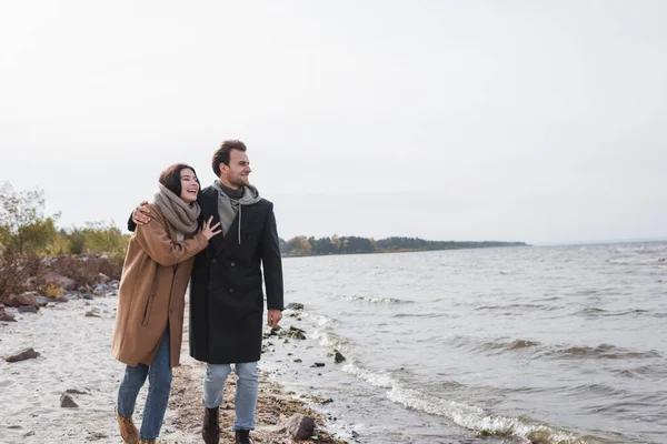 Joyful couple hugging and looking away during autumn walk along riverside — Stock Photo