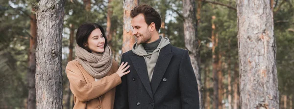 Pareja joven y feliz en traje de otoño mirándose en el parque, pancarta - foto de stock