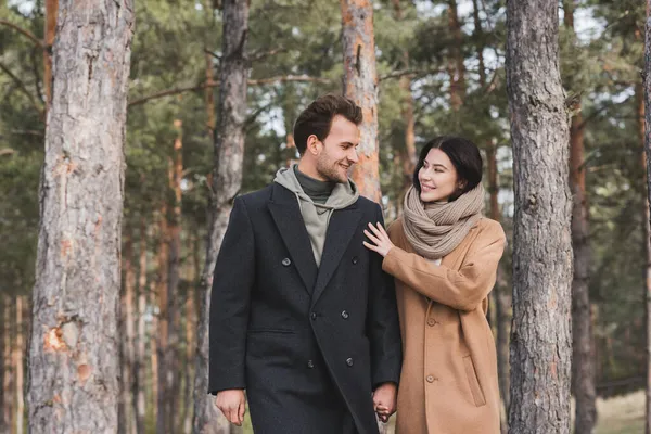 Cheerful woman touching shoulder of smiling boyfriend while walking in autumn park — Stock Photo
