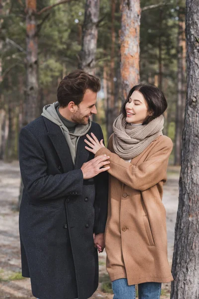 Pareja joven en abrigos de otoño sonriendo mientras camina en el bosque - foto de stock