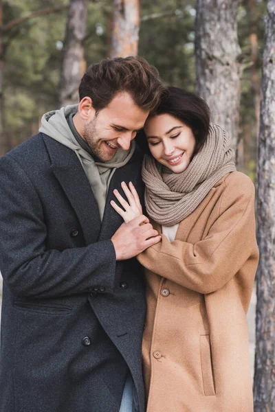 Joyful couple in autumn outfit embracing while walking in forest — Stock Photo