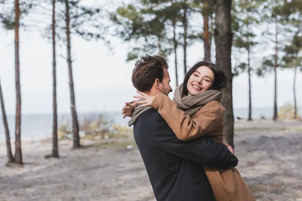 Excited woman in autumn coat hugging man while walking in autumn forest near river — Stock Photo