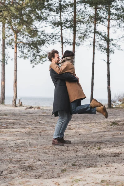 Vue latérale du jeune couple embrassant pendant la promenade d'automne dans la forêt près de la rivière — Photo de stock