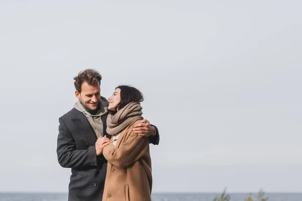 Happy man and woman in autumn coats hugging during walk outdoors — Stock Photo