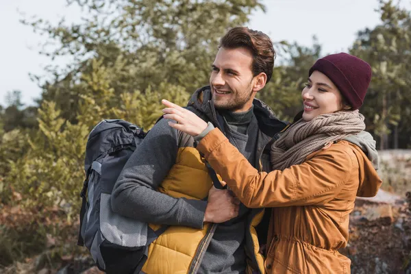 Smiling woman pointing with finger near man with backpack while walking outdoors — Stock Photo