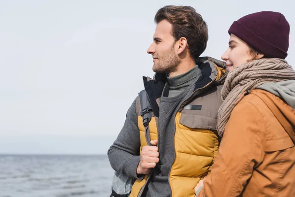 Pareja joven de turistas en traje de otoño mirando lejos cerca del mar - foto de stock