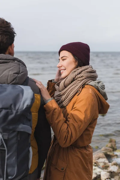 Junge Frau lächelt, während sie die Schulter eines Mannes mit Rucksack in Flussnähe berührt — Stockfoto