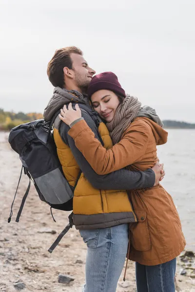 Felices jóvenes viajeros abrazando con los ojos cerrados al aire libre - foto de stock