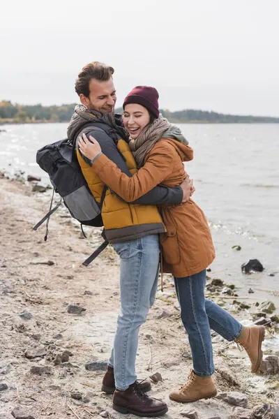 Freudiges Paar im Herbst-Outfit umarmt sich beim Spazierengehen an der Küste — Stockfoto