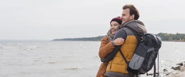 Couple joyeux regardant loin tout en embrassant près de la mer, bannière — Photo de stock