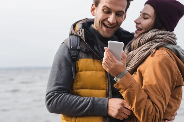 Woman showing mobile phone to cheerful boyfriend while walking outdoors — Stock Photo