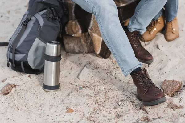 Par de caminhantes sentados perto de garrafa térmica e mochila durante a parada ao ar livre — Fotografia de Stock