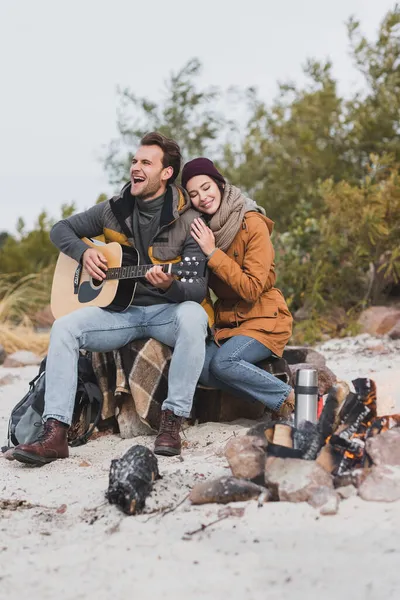 Mujer feliz con los ojos cerrados apoyándose en el hombre tocando la guitarra durante la parada en el paseo de otoño - foto de stock