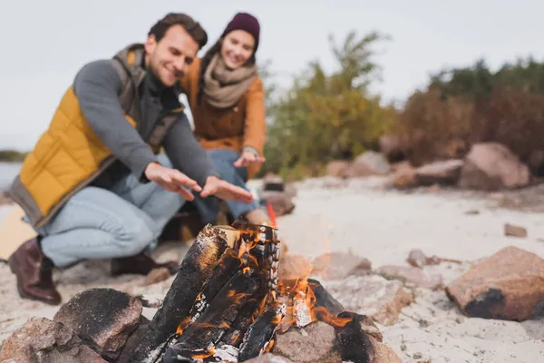 Couple flou de jeunes voyageurs se réchauffant près de feu de joie à l'extérieur — Photo de stock