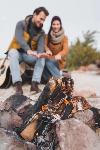 Selective focus of bonfire near blurred couple warming during autumn walk — Stock Photo