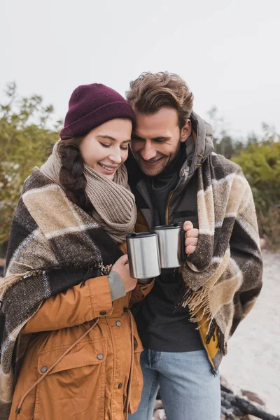 Zufriedene Reisende klirren mit Thermobechern, während sie unter karierter Decke im Freien stehen — Stockfoto