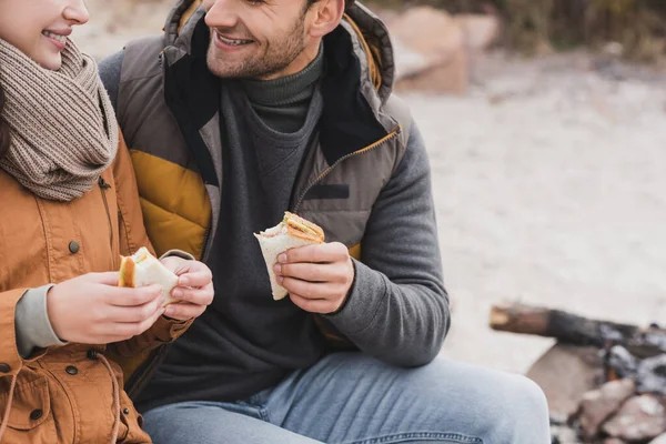 Vista recortada de la pareja sosteniendo sándwiches durante la parada al aire libre - foto de stock