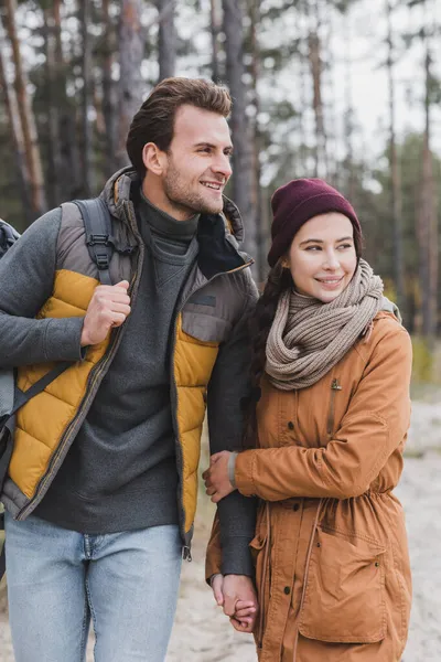 Happy young couple in autumn outfit looking away while walking in forest — Stock Photo